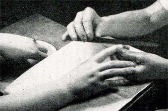 Рис. 391. Подпиливание ногтей правой руки. Тут мы видим также, как пальцы левой руки лежат уже в мягкой (мыльной) воде